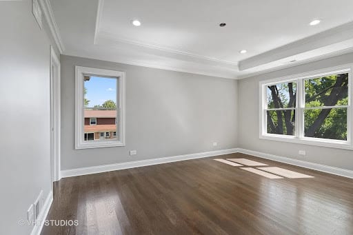 Empty room with dark hardwood floors, gray walls, and two windows