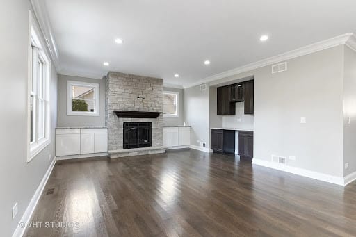 Open living room with stone fireplace, dark hardwood floors, and built-in cabinetry