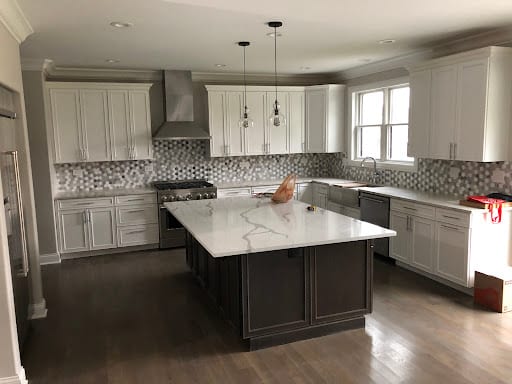 White shaker cabinets, large quartz island, and hexagon tile backsplash in remodeled kitchen