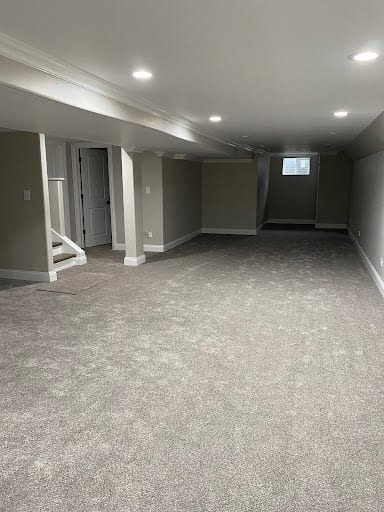 Freshly finished basement with gray carpet and recessed lighting