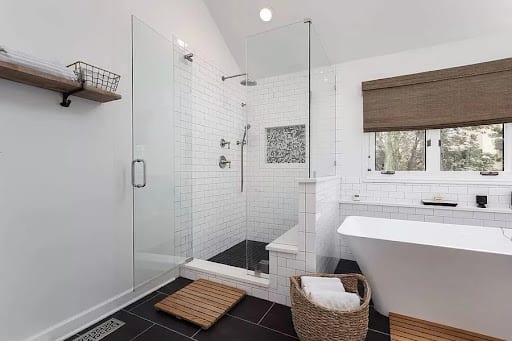 Walk-in glass shower and freestanding soaking tub in white tiled bathroom