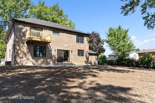 Two-story brick home addition with upper deck and freshly graded backyard