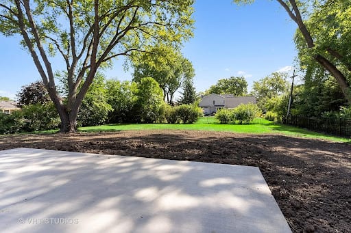 Freshly poured concrete patio slab in a spacious backyard with mature trees