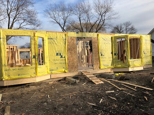 New home addition framing wrapped in yellow weather barrier under construction