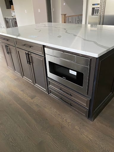 Kitchen island with dark cabinets, drawer microwave, and white quartz countertop