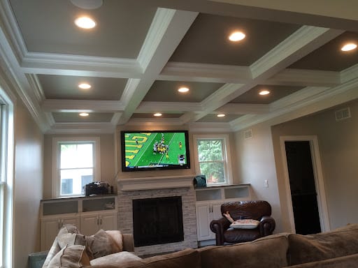 Living room with coffered ceiling, wall-mounted TV, and stone fireplace