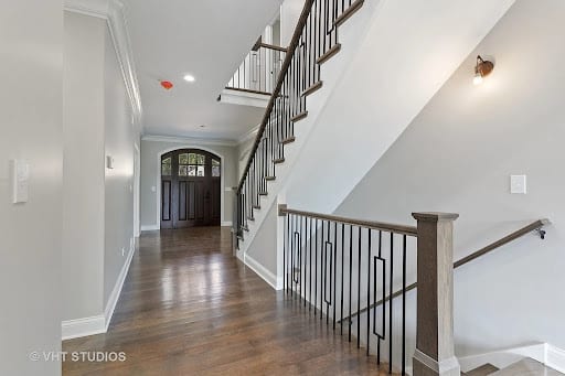 Bright foyer with dark hardwood floors, iron staircase railing, and arched front door