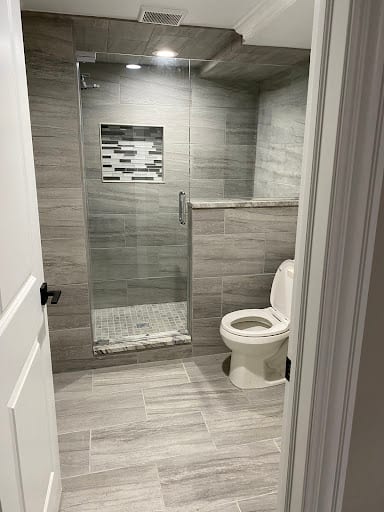 Walk-in glass shower with gray tile next to white toilet