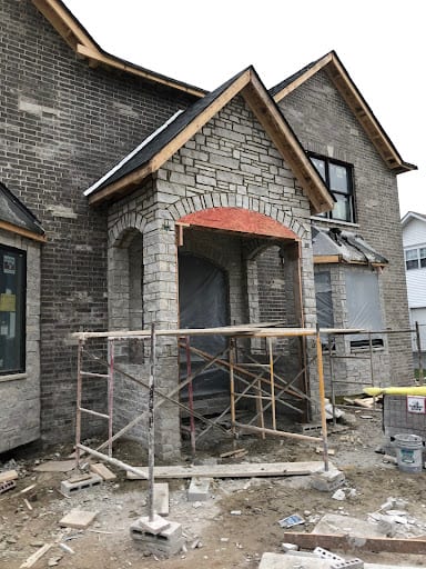 New brick home addition under construction with scaffolding and arched entryway
