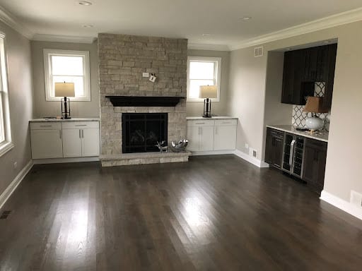 Open living room with stone fireplace, white built-ins, and dark hardwood floors