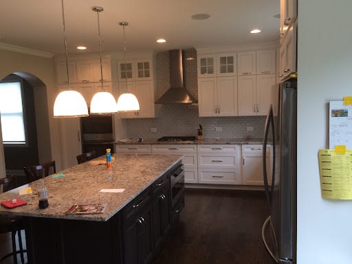 White shaker cabinets, granite island, and stainless range hood in remodeled kitchen