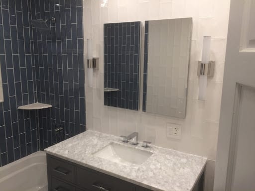Blue stacked tile shower with white marble vanity and wall sconces