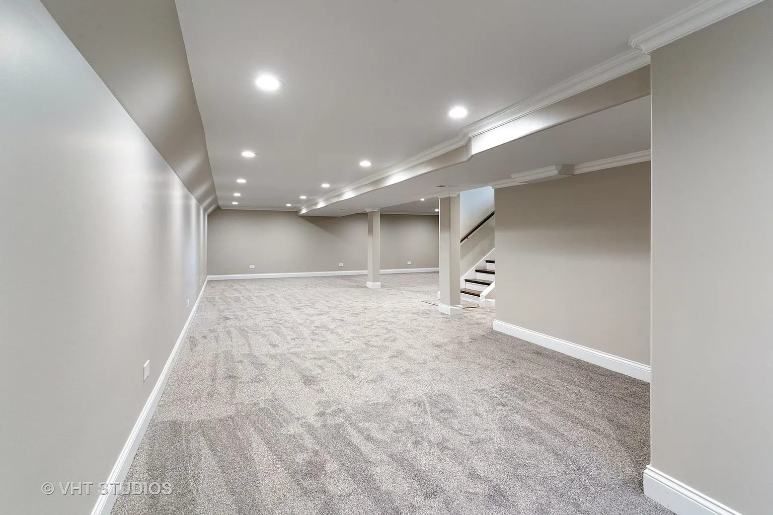Finished basement with gray carpet, recessed lighting, and staircase
