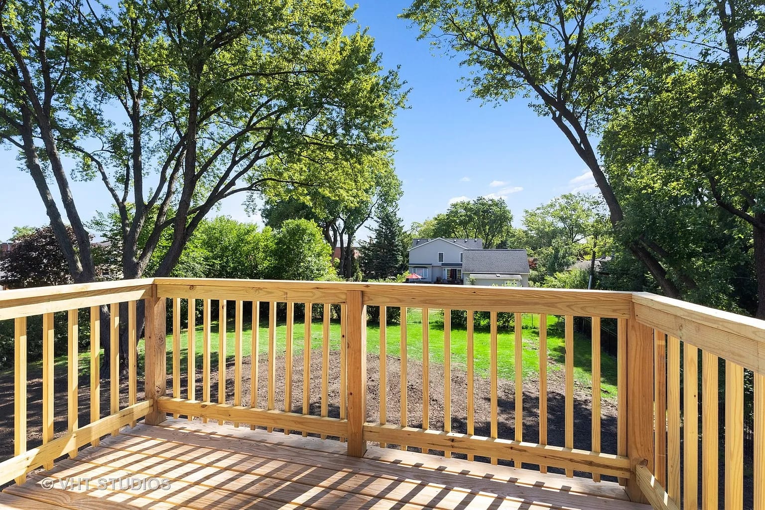 New wood deck with railings overlooking green backyard and trees